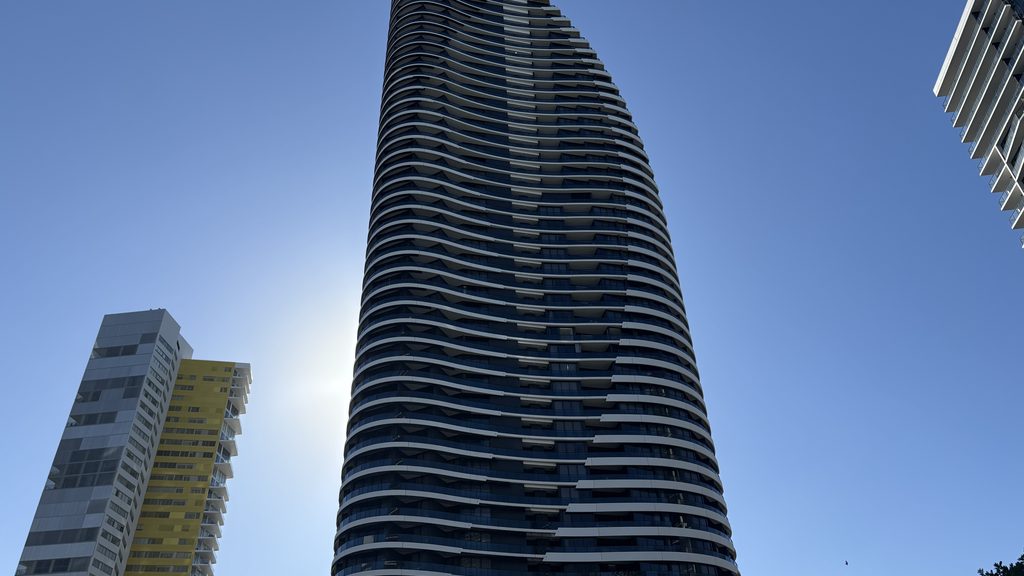 A curved high-rise apartment tower in Broadbeach against a clear blue sky